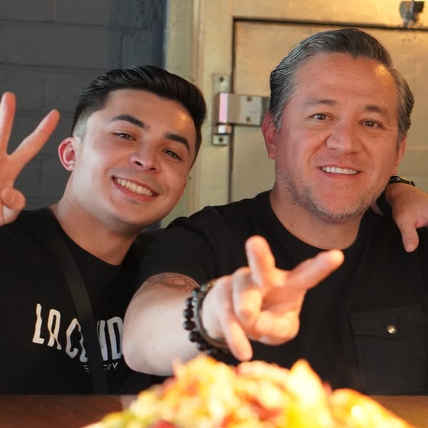 Two smiling men, one with a La Condesa Eatery shirt, making peace signs.