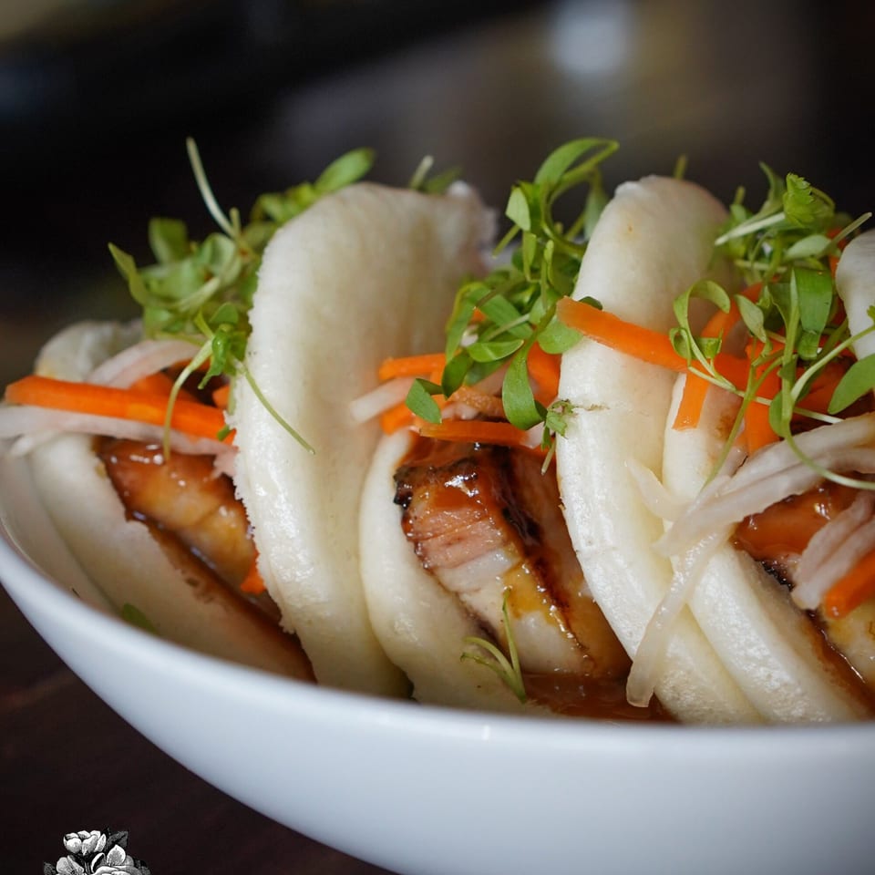 Close-up of La Condesa Eatery's bao buns filled with pork belly, carrots, and microgreens.