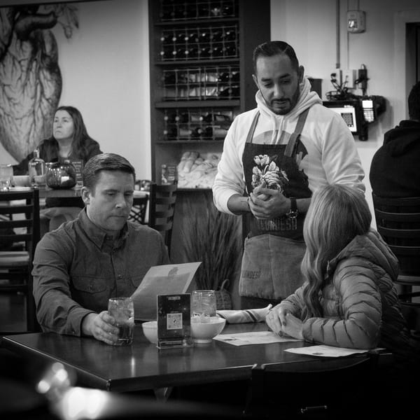 A La Condesa Eatery server in an apron stands by a table with two customers looking at menus.