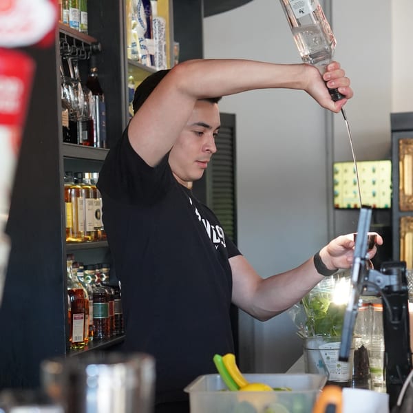 A bartender at La Condesa Eatery pours a drink, with bottles of liquor visible in the background.