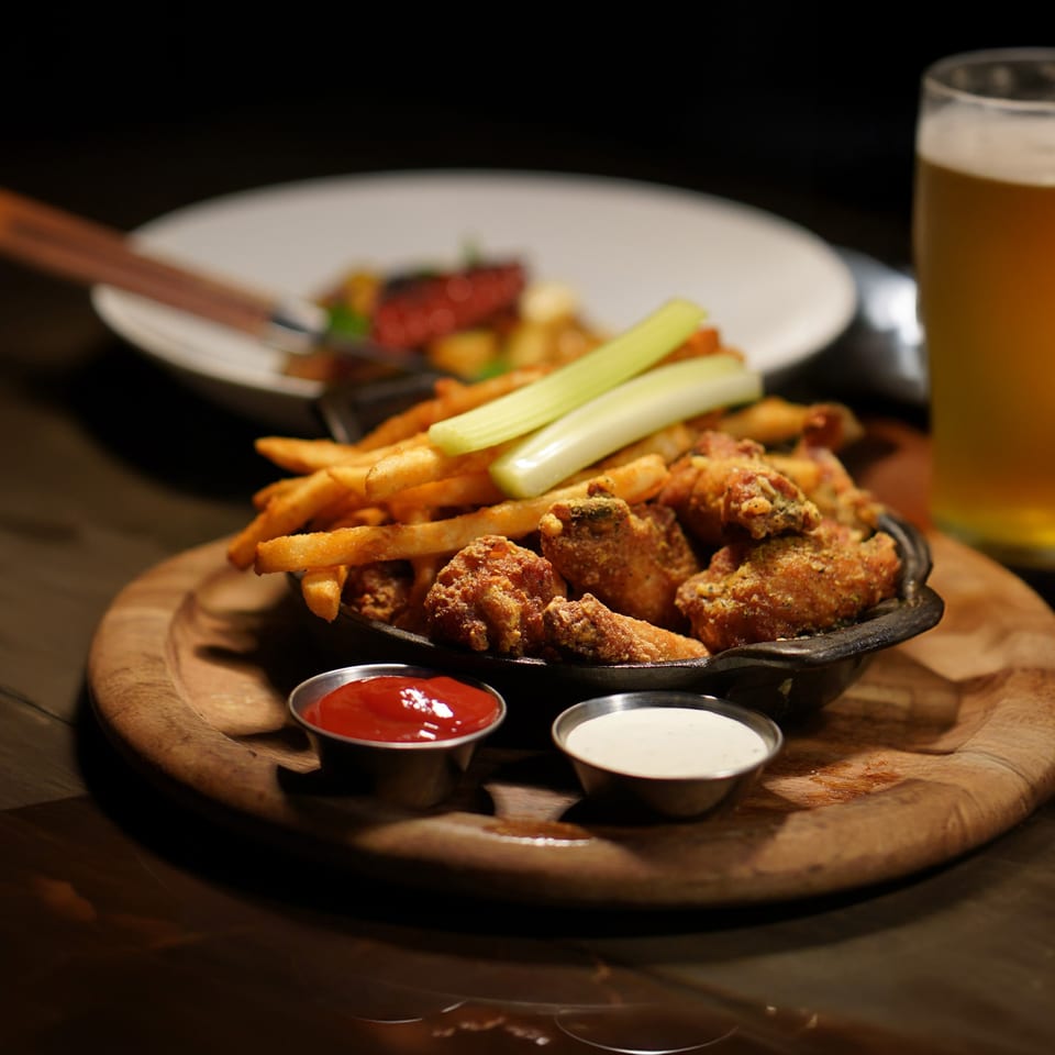 Fried chicken wings and french fries with celery sticks, ketchup, and ranch dressing.