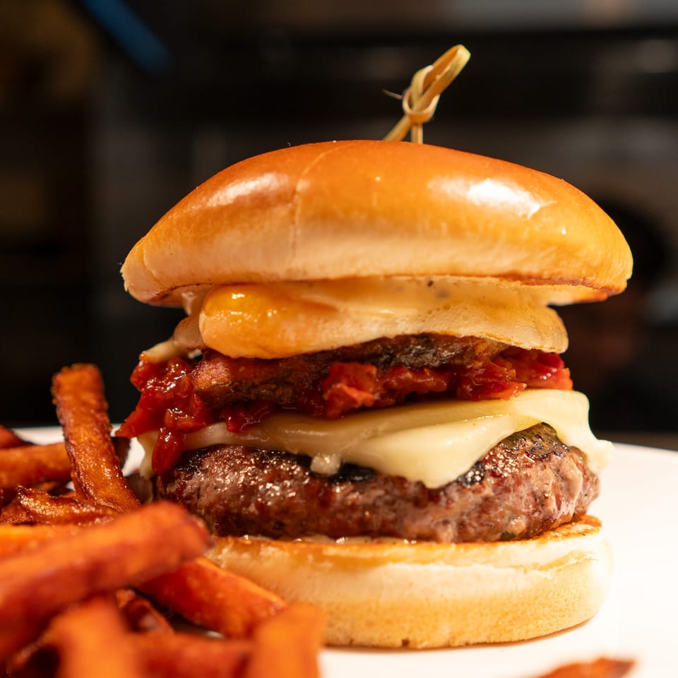 A gourmet burger with melted cheese, bacon jam, and sweet potato fries from La Condesa Eatery.