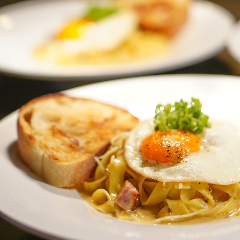 La Condesa Eatery's pasta dish with a fried egg, bacon, and toasted bread.