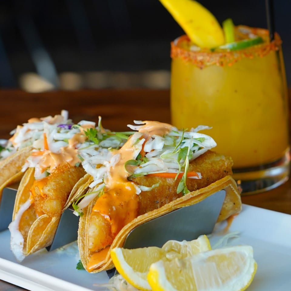 Crispy fish tacos with slaw and sauce, served with lemon wedges and a mango margarita.