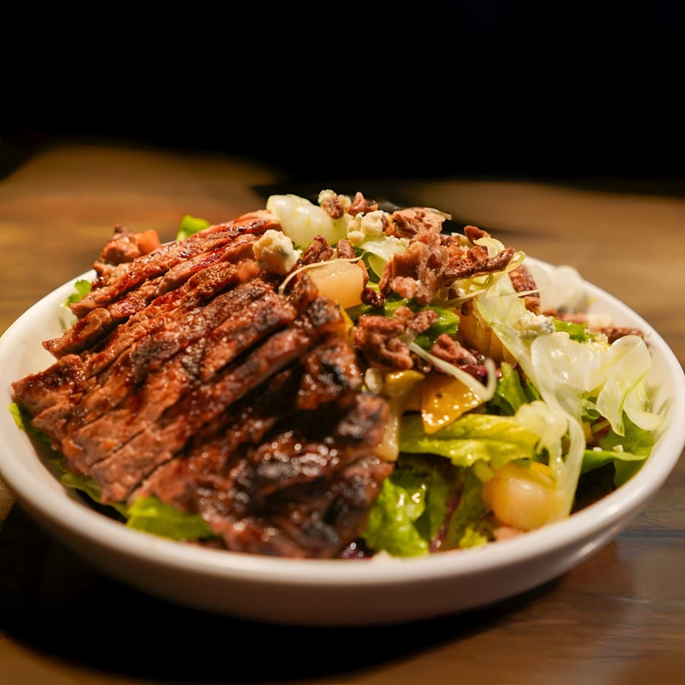 Grilled steak salad with lettuce, bacon, and cheese crumbles in a white bowl at La Condesa Eatery.