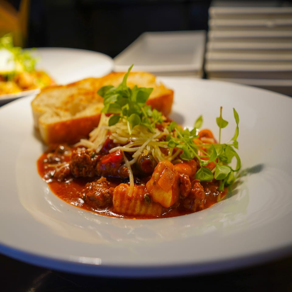 A white plate of gnocchi and meatballs in red sauce, topped with cheese and fresh greens.