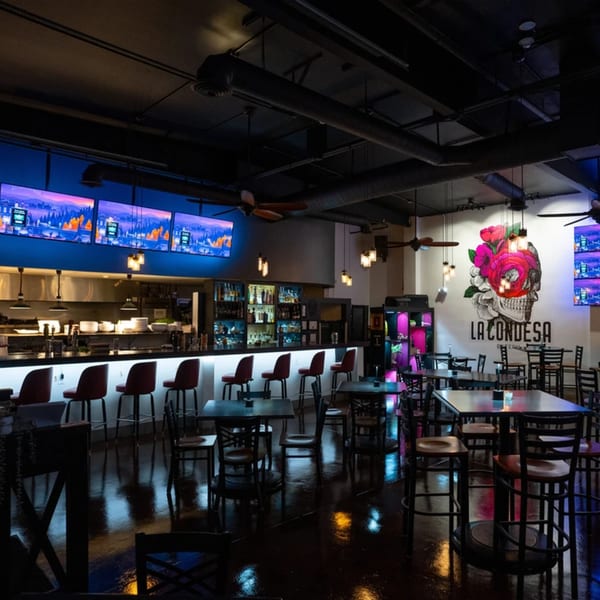 La Condesa Eatery's dark interior features a bar, dining tables, and a large skull mural.