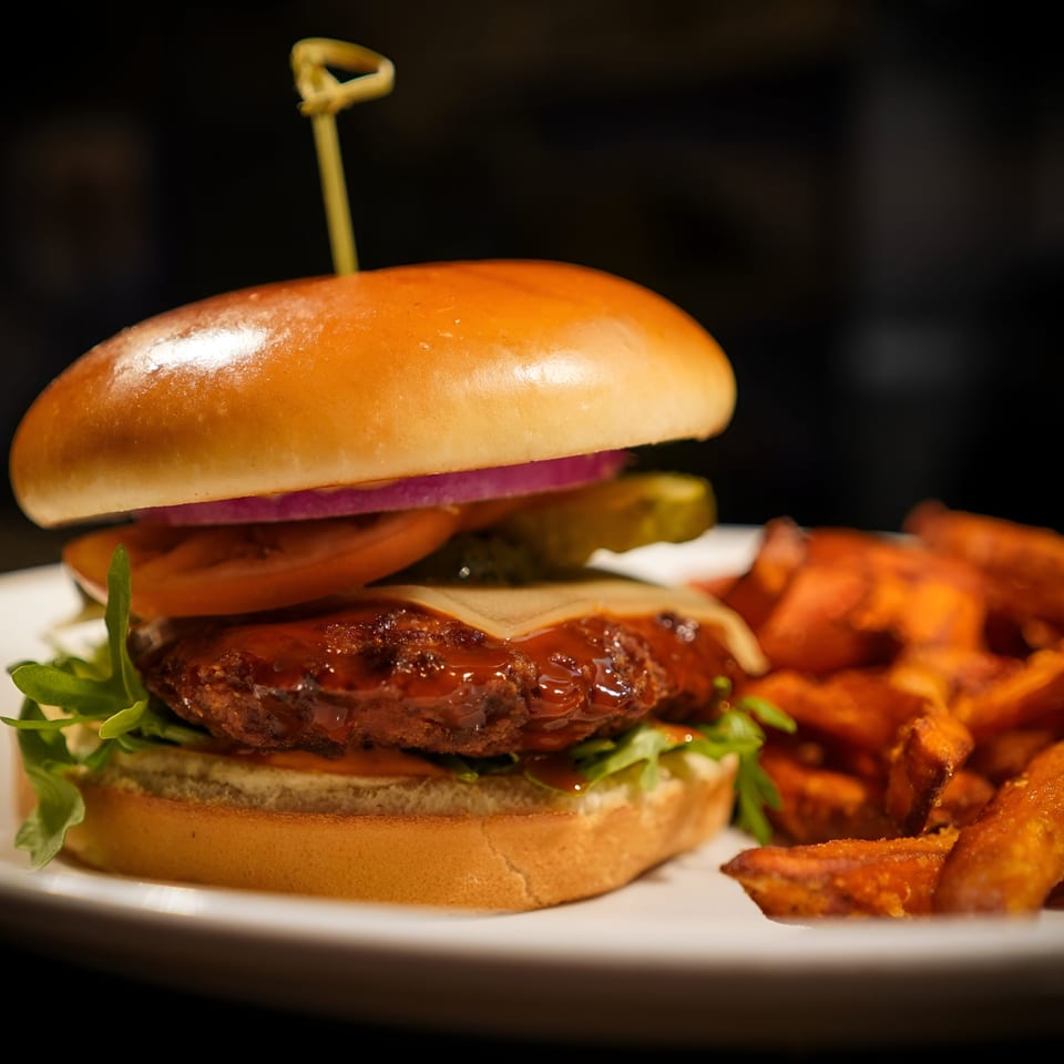 A La Condesa Eatery burger with sweet potato fries on a white plate.
