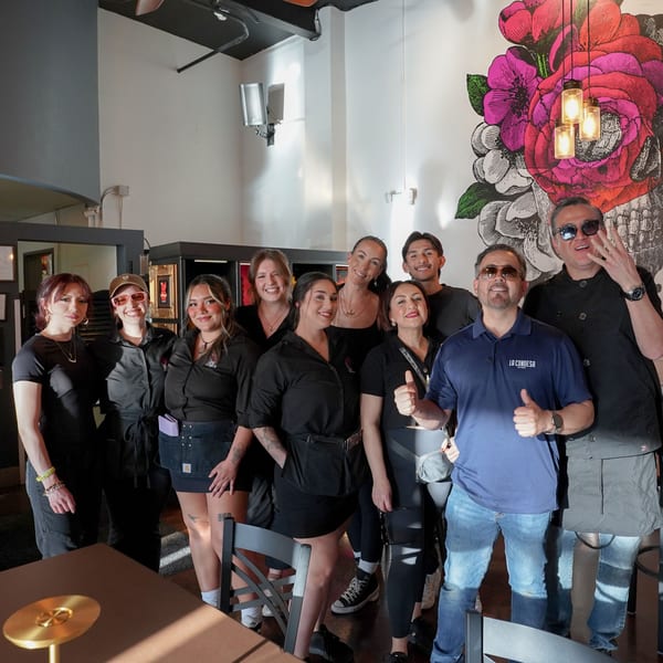 Restaurant staff, including men and women, pose together in front of a colorful floral mural.