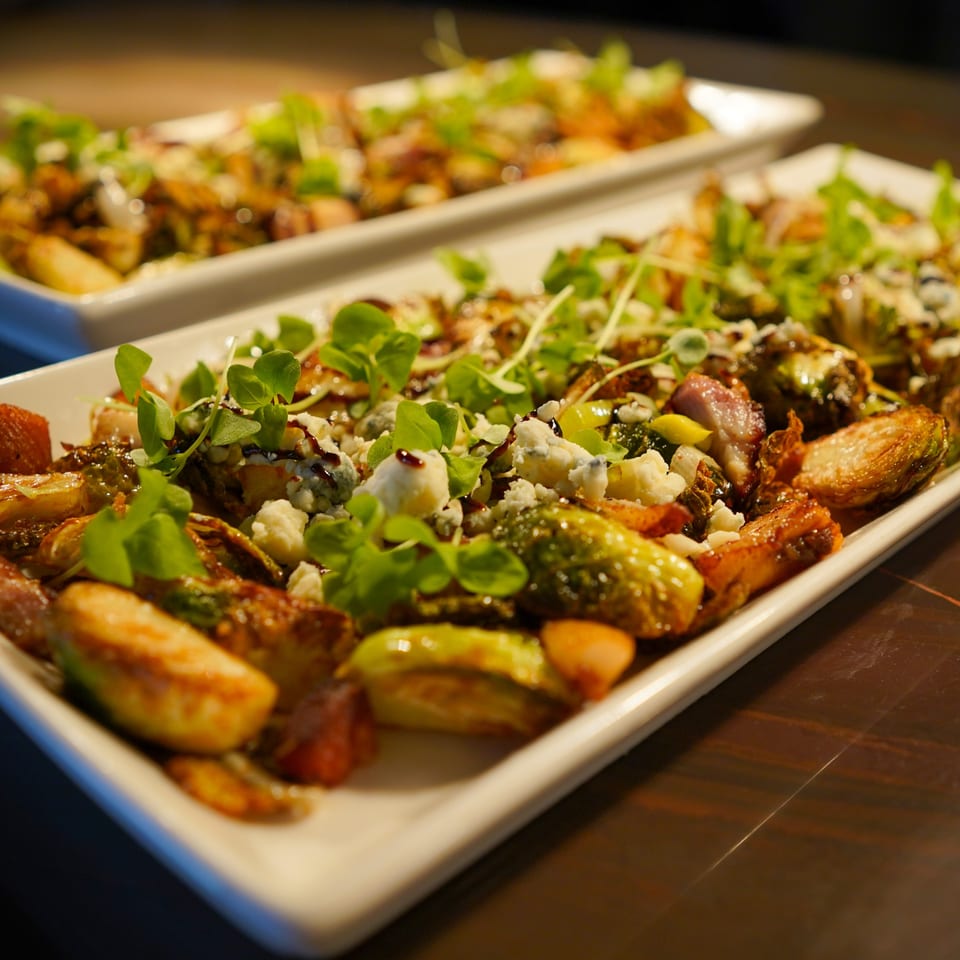 Two white rectangular plates filled with roasted Brussels sprouts, crumbled cheese, and microgreens.