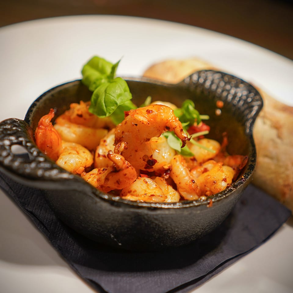 Spicy shrimp appetizer with basil in a black cast iron dish, served with bread.