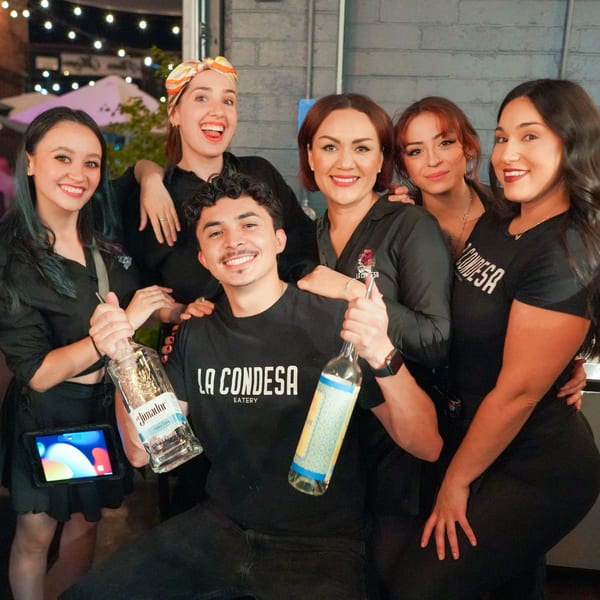 Six smiling La Condesa Eatery staff members, two holding bottles, posing together.