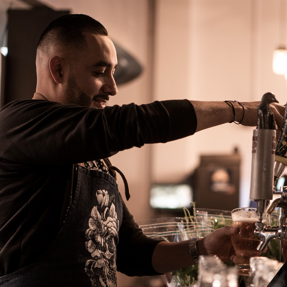 A bartender at La Condesa Eatery pours a beer from a tap into a glass.