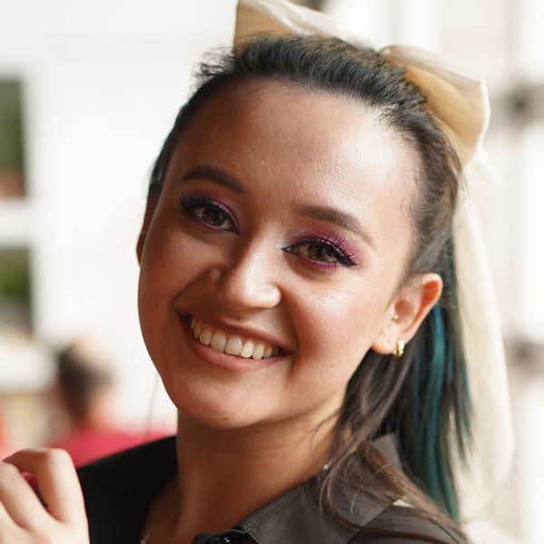 Smiling woman with dark hair tied back with a cream bow, wearing a black shirt.