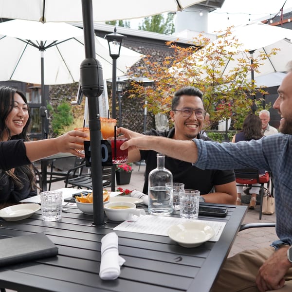 Three friends toasting colorful drinks on La Condesa Eatery's outdoor patio.
