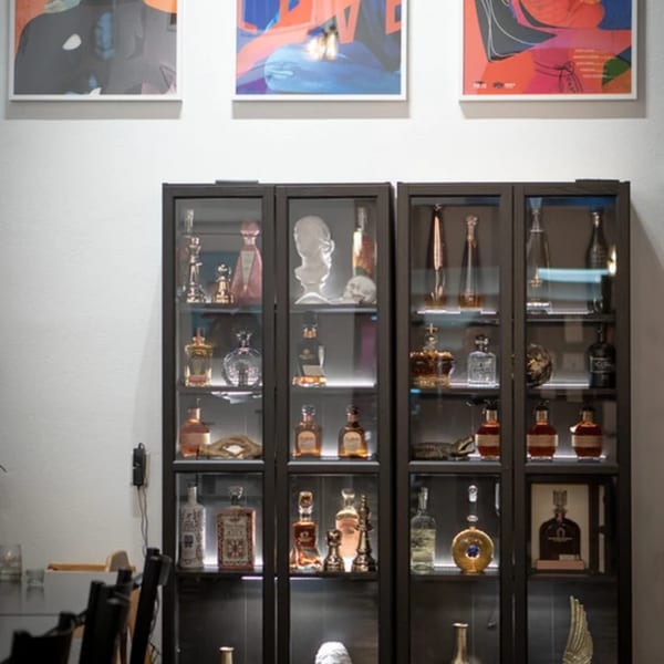 Three display cases filled with various liquor bottles and decorative items, with abstract art above.