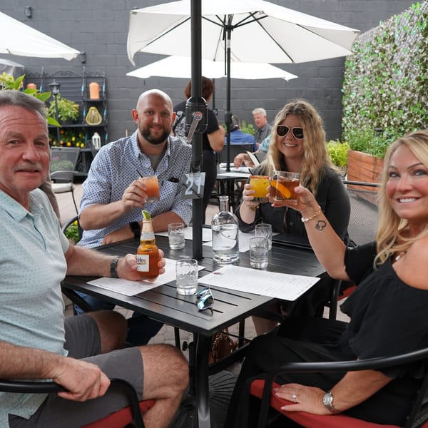 Four happy diners toast with drinks at an outdoor patio table at La Condesa Eatery.