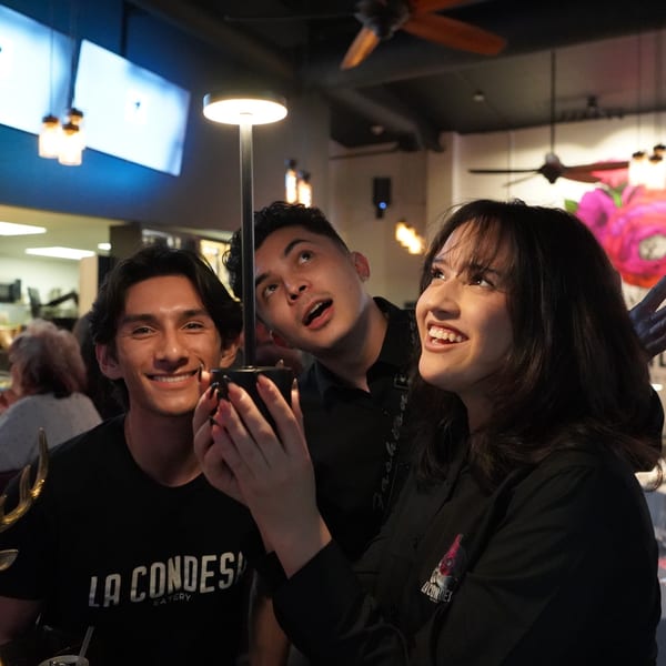 Three young adults, two smiling, one looking up, enjoying the vibrant atmosphere at La Condesa Eatery.