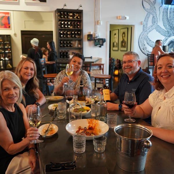 Six smiling people enjoying wine and food at a table in La Condesa Eatery.